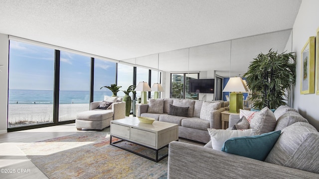 living room with a view of the beach, expansive windows, hardwood / wood-style flooring, a water view, and a textured ceiling