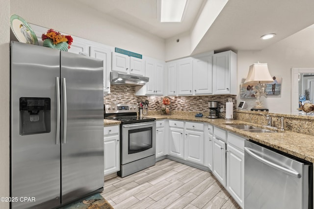 kitchen featuring stainless steel appliances, decorative backsplash, white cabinetry, a sink, and under cabinet range hood