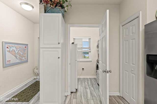 corridor featuring baseboards, wood finish floors, and stacked washer / drying machine