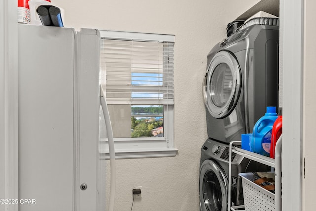 clothes washing area featuring a textured wall, laundry area, and stacked washer / drying machine