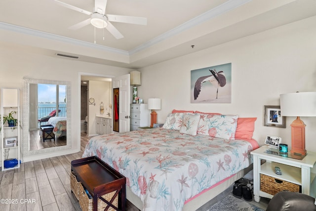 bedroom with a raised ceiling, visible vents, ornamental molding, wood tiled floor, and ensuite bath