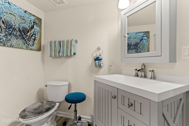 half bathroom featuring a textured wall, toilet, vanity, visible vents, and baseboards