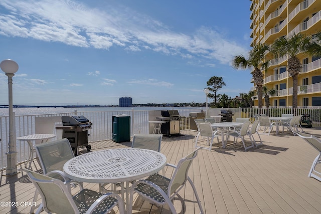 wooden terrace with outdoor dining area, a water view, and a grill