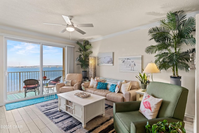 living room featuring a ceiling fan, ornamental molding, a water view, a textured ceiling, and light wood-style floors