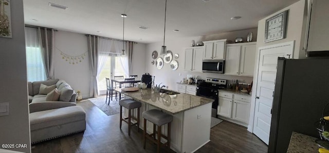 kitchen featuring a kitchen island with sink, stainless steel appliances, light stone counters, white cabinets, and a kitchen bar