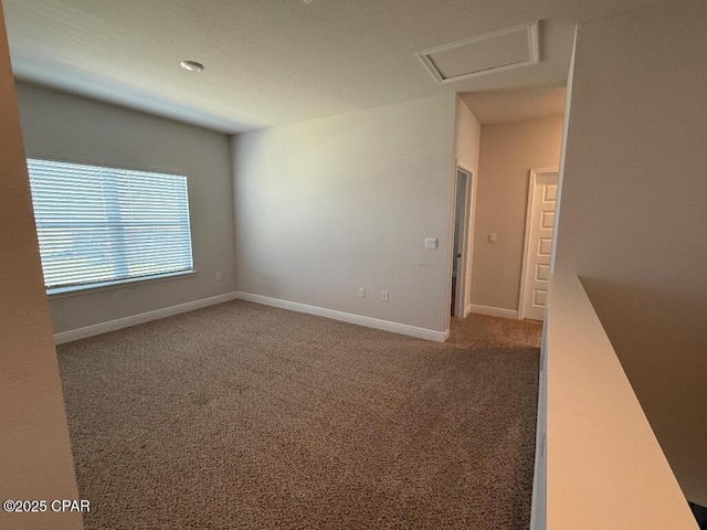 unfurnished room with carpet floors, attic access, and baseboards