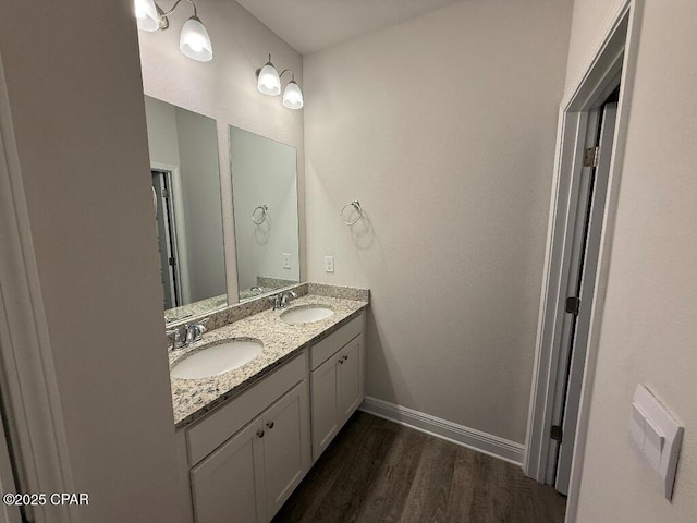 bathroom with double vanity, baseboards, a sink, and wood finished floors