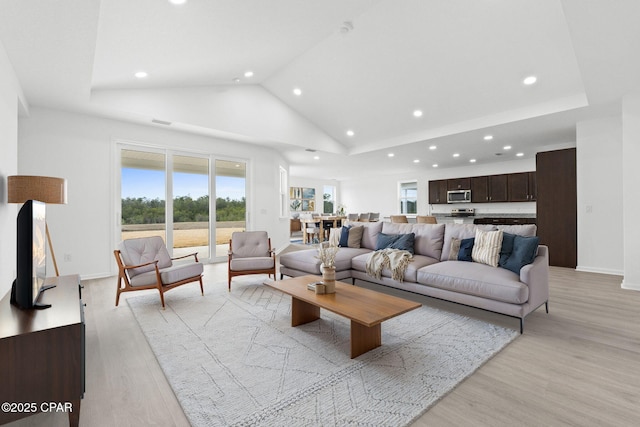 living room with plenty of natural light, high vaulted ceiling, light wood-style flooring, and baseboards