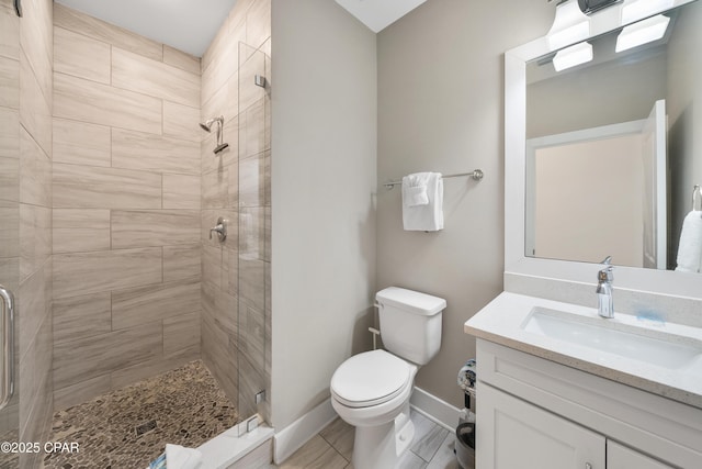 bathroom with toilet, a stall shower, baseboards, and vanity