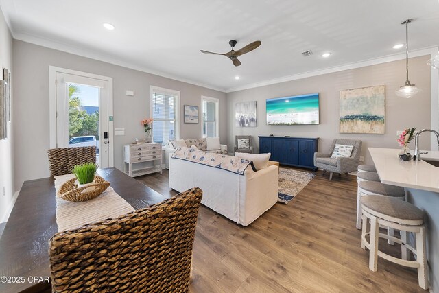 living room with hardwood / wood-style floors, crown molding, sink, and ceiling fan