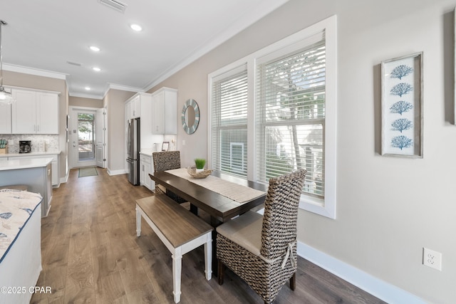 dining room with baseboards, wood finished floors, visible vents, and crown molding