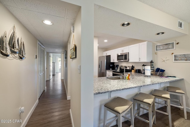 kitchen featuring a kitchen bar, kitchen peninsula, stainless steel appliances, light stone countertops, and white cabinets