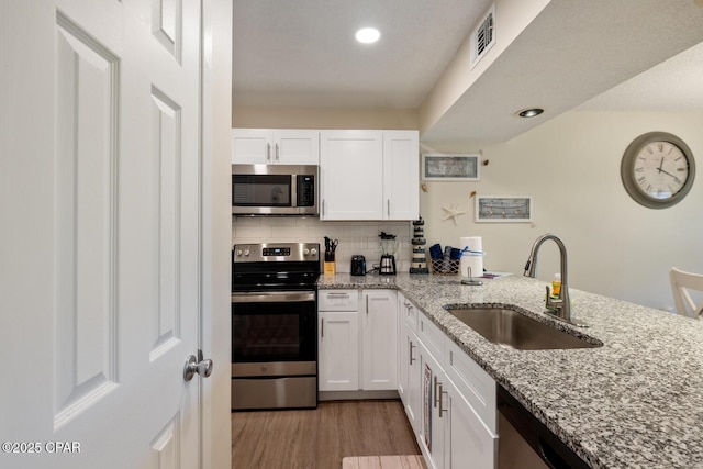 kitchen with sink, light stone countertops, white cabinets, and appliances with stainless steel finishes