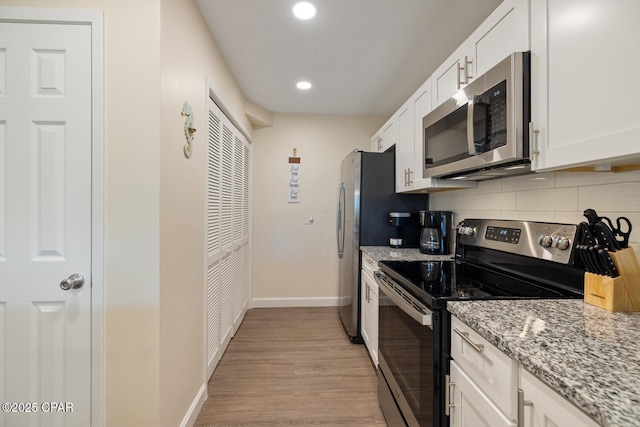 kitchen with appliances with stainless steel finishes, tasteful backsplash, white cabinets, light stone countertops, and light wood-type flooring