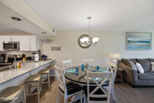 dining space featuring a notable chandelier, sink, a textured ceiling, and dark hardwood / wood-style floors