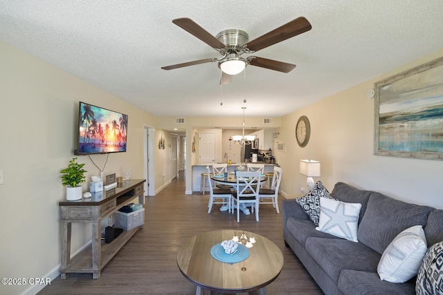 living room featuring dark hardwood / wood-style flooring, ceiling fan with notable chandelier, and a textured ceiling