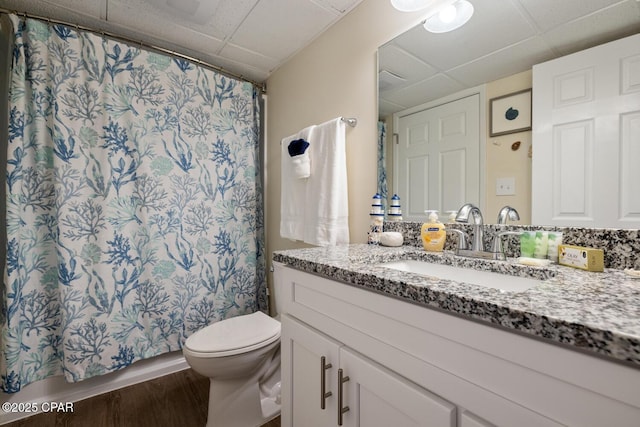 bathroom with wood-type flooring, a paneled ceiling, vanity, and toilet