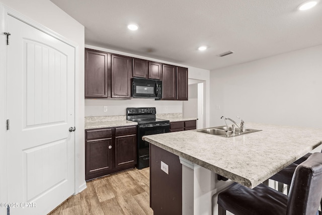 kitchen featuring a breakfast bar area, visible vents, light wood-style flooring, a sink, and black appliances