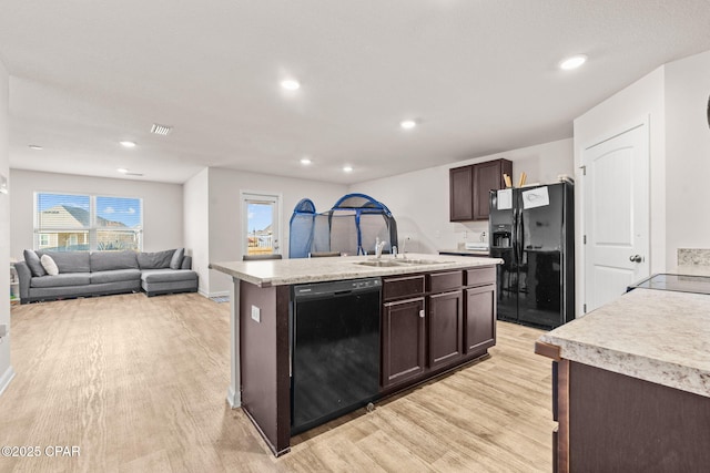 kitchen featuring dark brown cabinets, light countertops, light wood-style flooring, black appliances, and a kitchen island with sink