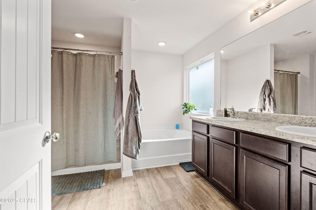 full bathroom featuring a sink, wood finished floors, double vanity, and a bath