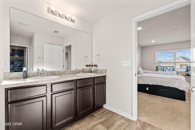 ensuite bathroom with visible vents, a sink, wood finished floors, connected bathroom, and double vanity