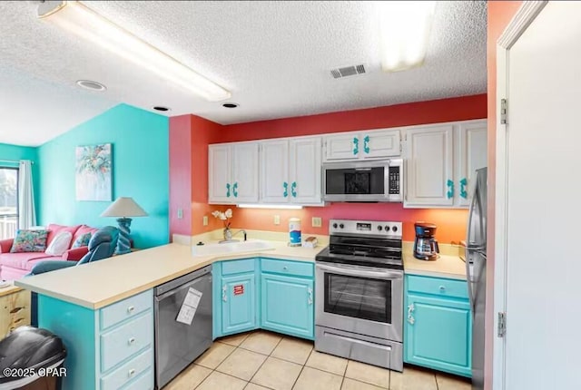 kitchen featuring sink, light tile patterned floors, appliances with stainless steel finishes, white cabinets, and kitchen peninsula