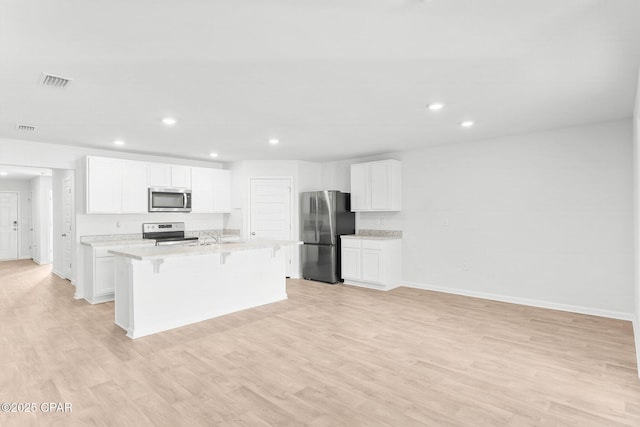 kitchen featuring stainless steel appliances, a kitchen breakfast bar, an island with sink, and white cabinets