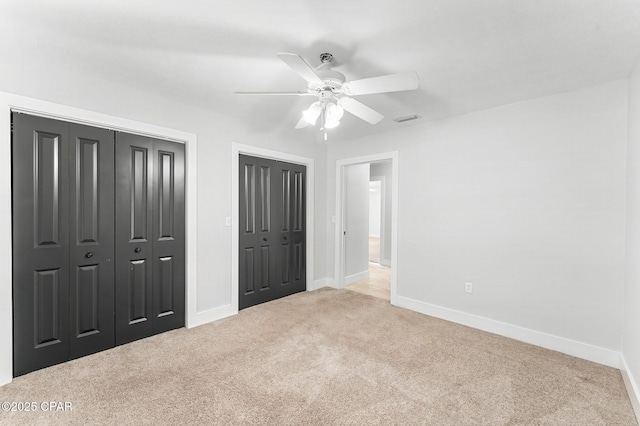 unfurnished bedroom with multiple closets, light carpet, and ceiling fan