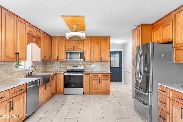 kitchen with pendant lighting, sink, decorative backsplash, light stone counters, and stainless steel appliances