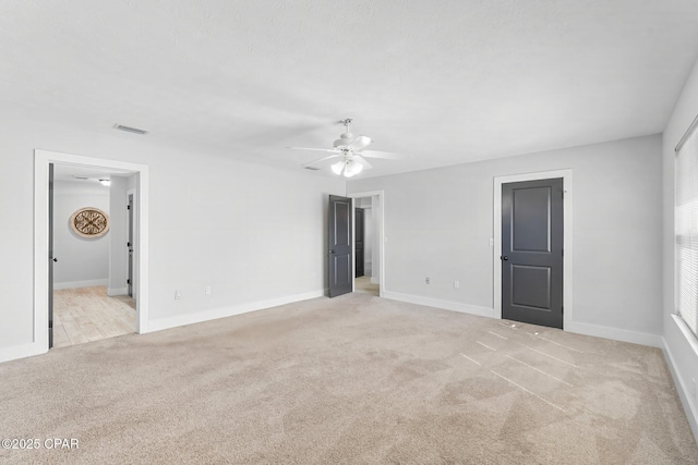 spare room with a ceiling fan, light colored carpet, visible vents, and baseboards