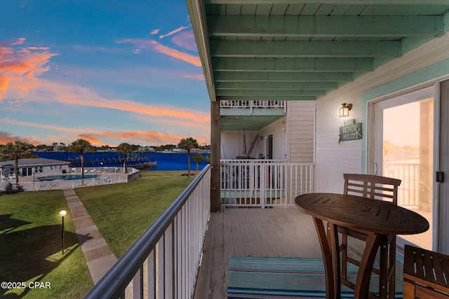 deck at dusk featuring a lawn and a water view