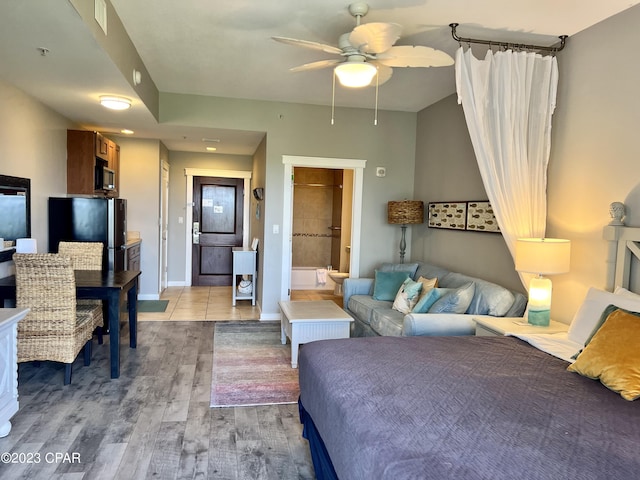 bedroom featuring stainless steel refrigerator, ensuite bath, and light hardwood / wood-style flooring