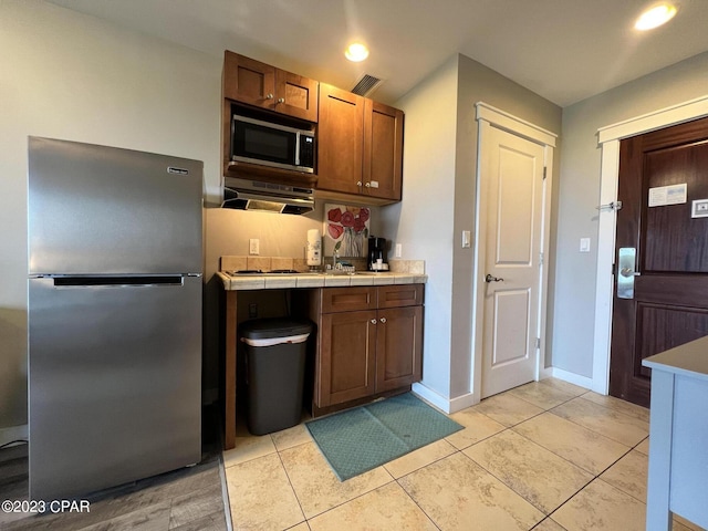 kitchen with light tile patterned floors, stainless steel appliances, visible vents, baseboards, and range hood