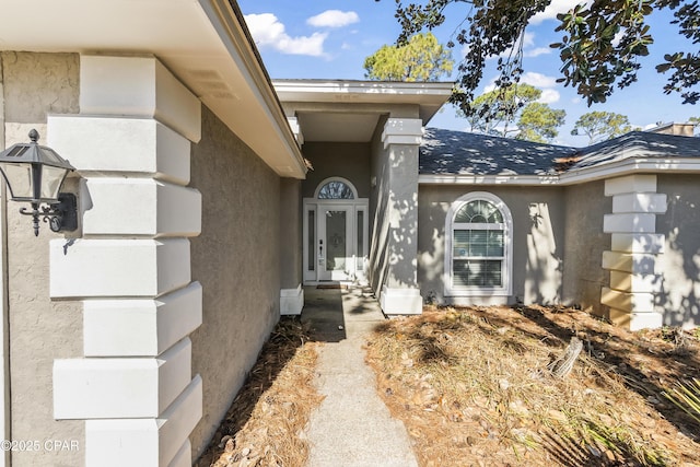 view of exterior entry with a shingled roof and stucco siding