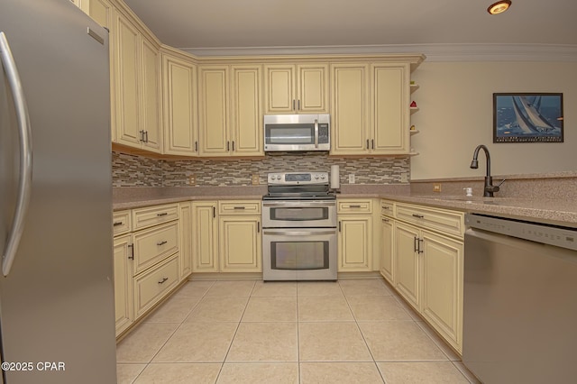 kitchen with sink, light tile patterned floors, appliances with stainless steel finishes, ornamental molding, and cream cabinets