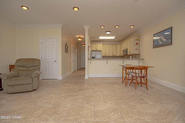 kitchen featuring crown molding, a breakfast bar, appliances with stainless steel finishes, cream cabinets, and kitchen peninsula