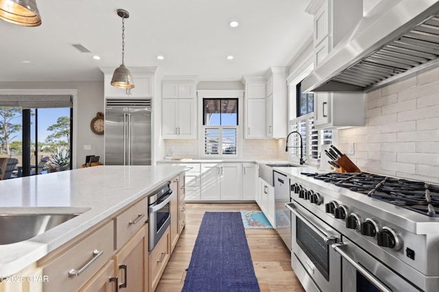 kitchen featuring hanging light fixtures, high end appliances, ventilation hood, light stone countertops, and white cabinets