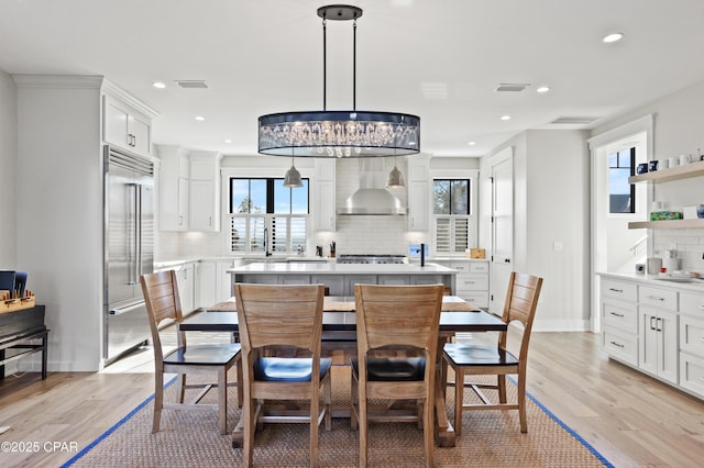 kitchen featuring wall chimney exhaust hood, appliances with stainless steel finishes, decorative light fixtures, and white cabinets