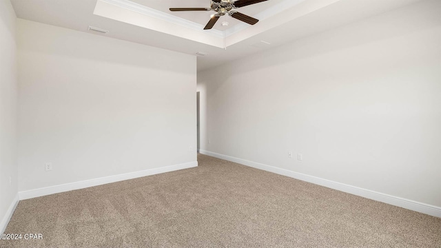 empty room with a tray ceiling, carpet floors, ornamental molding, and ceiling fan