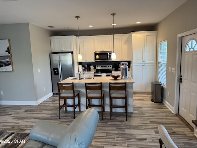 kitchen with sink, appliances with stainless steel finishes, hanging light fixtures, an island with sink, and white cabinets