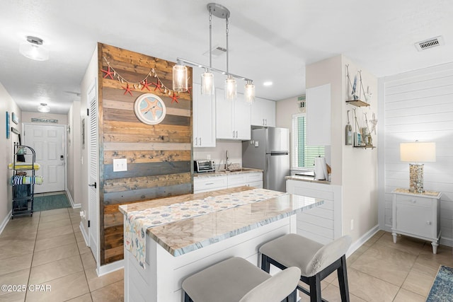 kitchen with wood walls, white cabinets, stainless steel fridge, hanging light fixtures, and light stone countertops