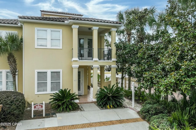 view of front of home featuring a balcony, a tile roof, and stucco siding