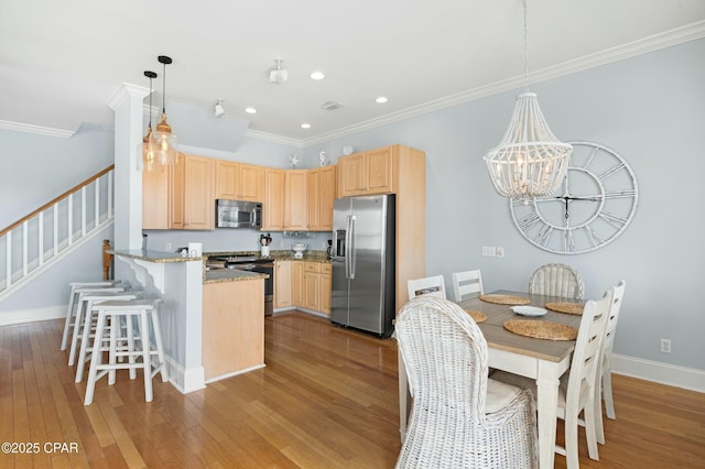 kitchen featuring appliances with stainless steel finishes, decorative light fixtures, light stone countertops, light brown cabinetry, and light wood-style floors