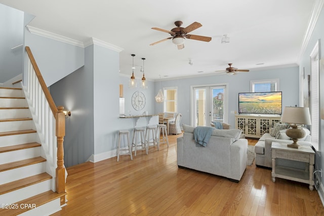 living room featuring light wood-style flooring, a ceiling fan, baseboards, stairs, and ornamental molding