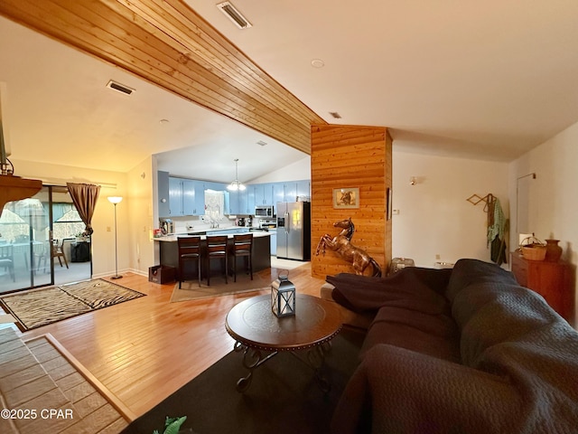 living area with visible vents, lofted ceiling, wood walls, and light wood finished floors