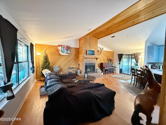 living room with lofted ceiling, a large fireplace, light wood-type flooring, and wood walls