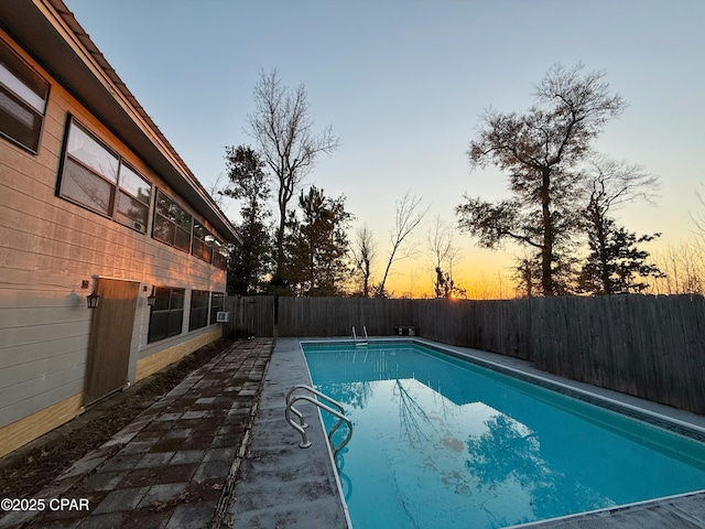 pool at dusk featuring a fenced in pool, a fenced backyard, and a patio area