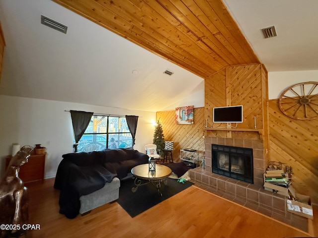 living room with wood finished floors, visible vents, vaulted ceiling, wood walls, and a tiled fireplace