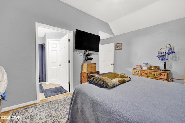 bedroom with connected bathroom, hardwood / wood-style floors, and vaulted ceiling