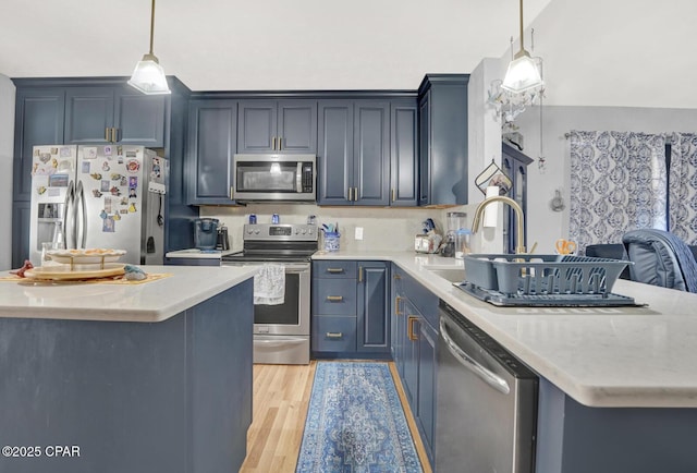 kitchen featuring pendant lighting, sink, appliances with stainless steel finishes, a center island, and light hardwood / wood-style floors